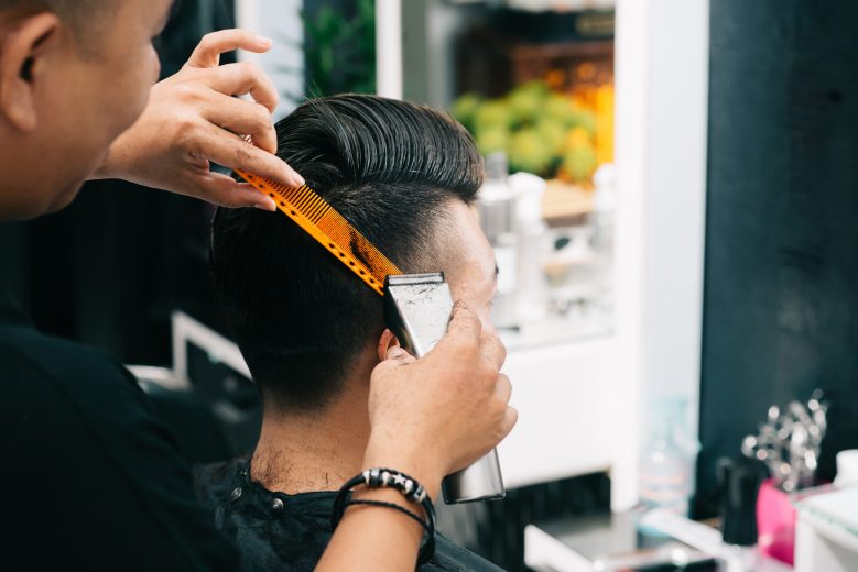 Close-up image of barber using trimmer when doing stylish haircut for a young man